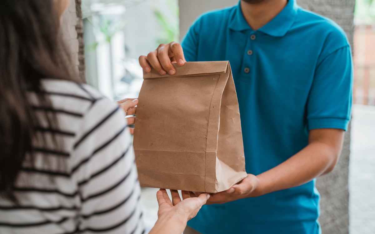 Vemos una imagen de una persona entregando un delivery a otra persona, en referencia a los modelos de negocio que existen para emprender un negocio de comida. 