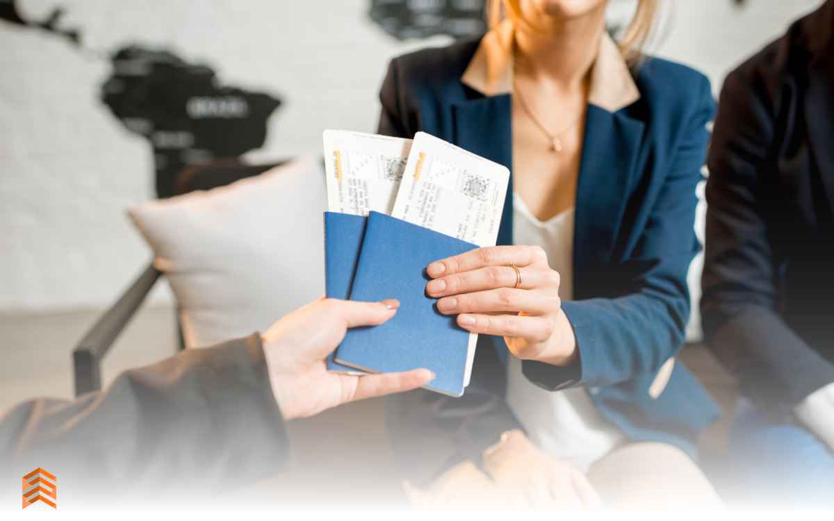 Vemos una imagen de una persona entregando a otra persona dos boletos de avión, en relación la elección de nombres de agencias de viaje.